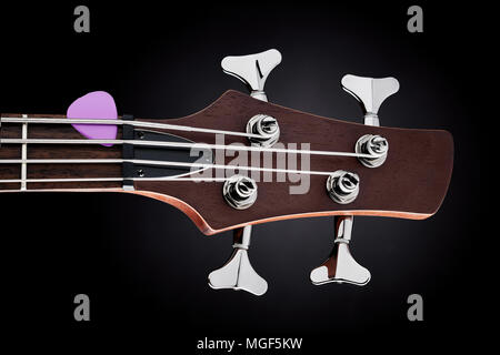 close-up studio shot of a maroon bass guitar head-stock with purple pick on black background Stock Photo