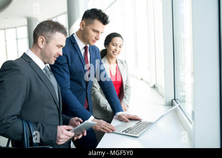 Busy concentrated business team watching online presentation on laptop and analyzing data in corridor Stock Photo