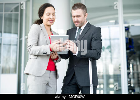 Positive confident multiethnic managers discussing sales and making forecast while analyzing report on tablet in office hall Stock Photo