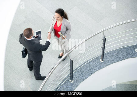 Directly above view of confident multiethnic business partners holding personal staff while shaking hands in hall Stock Photo