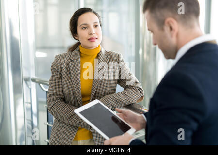 Serious confident purposeful young mixed race businesswoman leaning on railing and listening to colleagues idea while they brainstorming on office Stock Photo