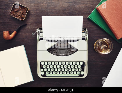 Author table. Vintage f type typewriter, blank paper, pipe, books, tobacco box and a glass of whiskey on a wooden table. Stock Photo