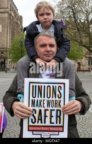 Manchester, UK. 28 April 2018. A father carries his young son on his shoulders whilst his sign reads 'Unions make Work Safer' at the International Workers Memoriial Day rally in Manchester city centre. This day (April 28th) each year commemorates all workers rights worldwide. Credit: SOPA Images Limited/Alamy Live News Stock Photo