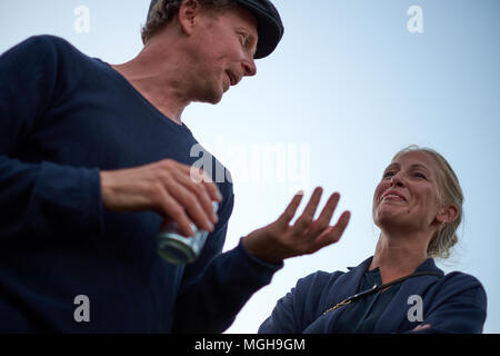 Gothenburg / Sweden - August 13th 2015: Two people stand, against a clear blue evening sky, smiling, talking and having fun together Stock Photo