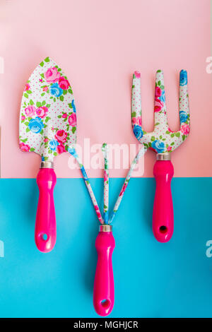 Small garden shovel and rake on a blue and pink background.set of rake steel and shovel isolated. Metal gardening hoe weeding chisel trowel and rake agriculture concept. Stock Photo