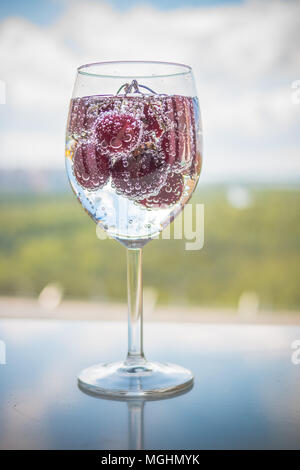 sweet cherry in a glass of sparkling soda water, healthy drinking concept.Refreshing summer drinks.summer bright fruit cocktails, lemonade on blur background. Vertical image Stock Photo