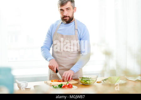 Waist-up portrait shot of confident bearded food vlogger wearing apron looking at camera while explaining his followers how to prepare delicious dish, Stock Photo