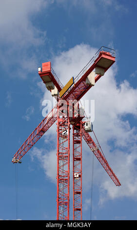 Two red cranes forming a large X in front of a clear blue sky with fluffy white clouds Stock Photo