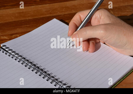 Woman with pen in hand, poised to write in a spiral bound notebook Stock Photo