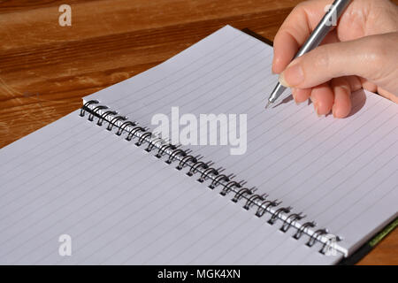 Woman with pen in hand, poised to write in a spiral bound notebook Stock Photo