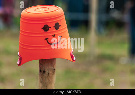 a orange bucket with a drawn face placed on top of a wooden pole Stock Photo