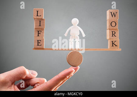 A Person's Hand With Human Figure Standing Between Work And Life Wooden Blocks On Seesaw Stock Photo