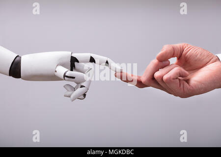 Robot Touching Human Finger Against Gray Background Stock Photo