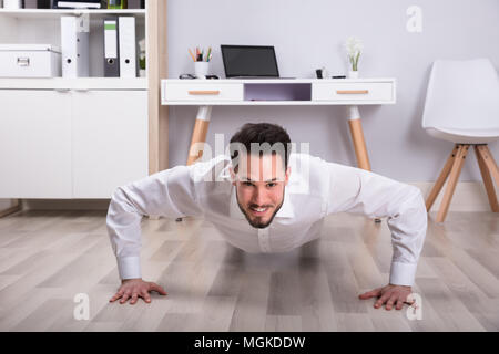 Portrait Of A Smiling Young Businessman Doing Push Up On Floor In Office Stock Photo