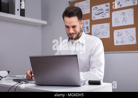 Happy Young Male Designer Using Laptop In Office Stock Photo