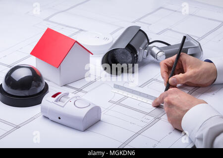 Close-up Of An Architect's Hand Drawing Blueprint Near Security Equipments And House Model Stock Photo