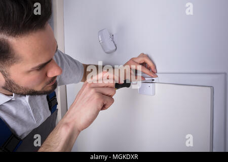 Young Male Technician Installing Security System Door Sensor On Wall Using Screwdriver Stock Photo