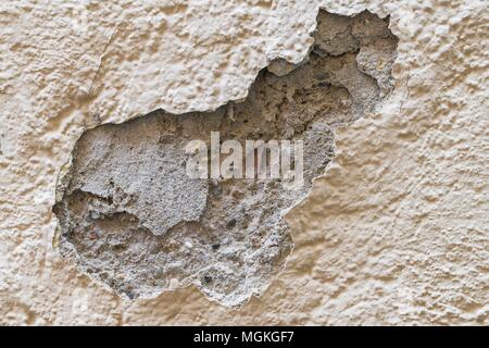 A damaged house wall and flaked exterior plaster with a large hole Stock Photo