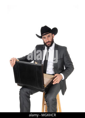 A handsome young business man sitting with his briefcase on his knees wearing a black cowboy hat, isolated for white background Stock Photo