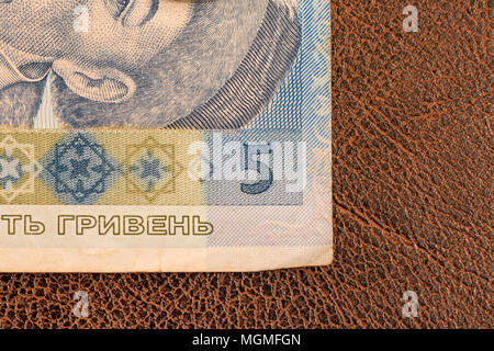 KIEV, UKRAINE - DECEMBER 19, 2014: Ukrainian paper money, hryvnia, lays down on brown imitation leather with patterns. Partial macro photo of the corner of the banknote. Bill of five Stock Photo