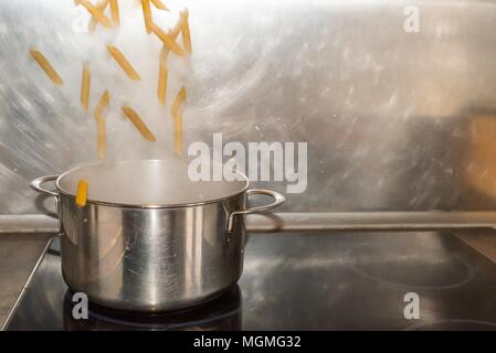 Penne Rigate noodles fall into a saucepan with boiling water Stock Photo