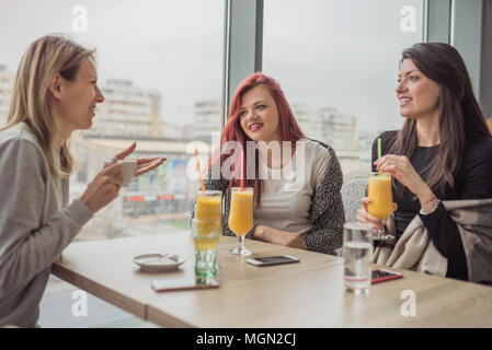 Portrait of three young beautiful women using mobile phone at coffee shop. Three young female friends enjoying together in a restaurant laughing, talk Stock Photo