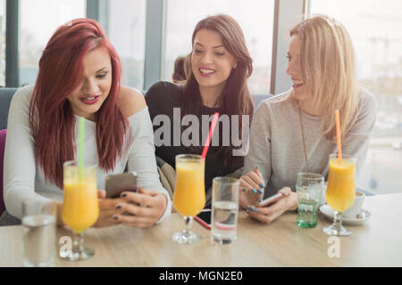 Portrait of three young beautiful women using mobile phone at coffee shop. Three young female friends enjoying together in a restaurant laughing, talk Stock Photo