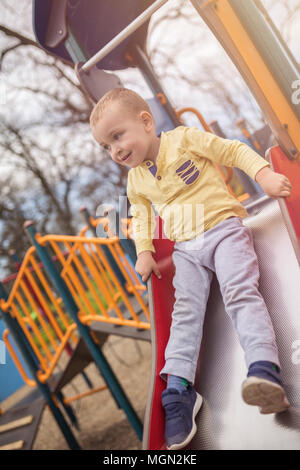 Adorable little boy having fun on playground. Active sport leisure for kids outdoor in park. Little boy with blue eyes in yellow shirt playing and hav Stock Photo