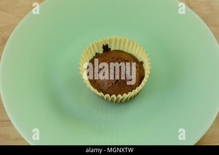 One burned cornmeal muffin in paper muffin cup on green plate Stock Photo
