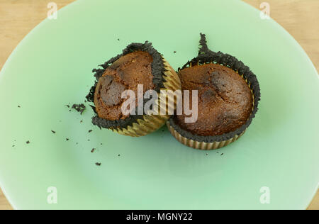 Two burned corn muffins with burned paper muffin cups on green plate Stock Photo