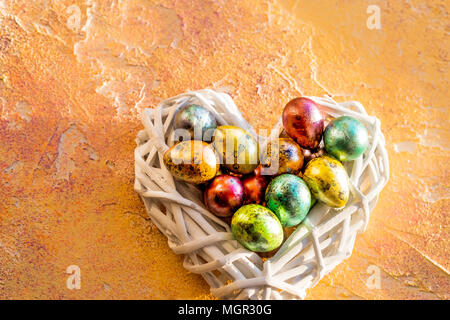 Colorful easter eggs in white nwst, heart on yellow background. Flat lay, top view. Happy Easter. Quail egg in nest, spring and easter holiday decoration. Stock Photo