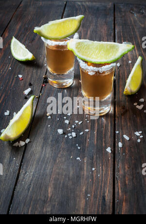 Shots of gold tequila with lime slices and salt on wood background. Stock Photo