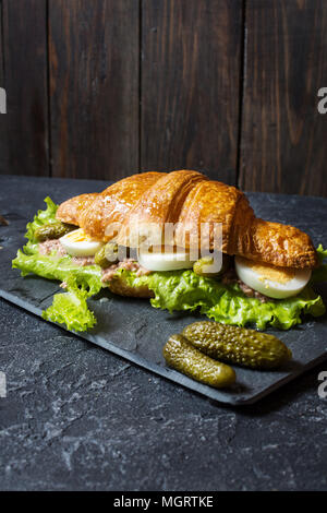 Croissant sandwich with tuna, hard boiled egg, salad and cucumber on stone table. Stock Photo