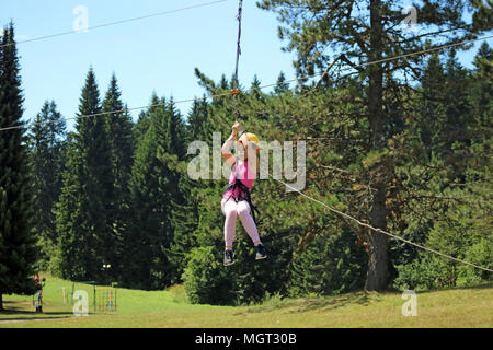 Little girl sliding on a zip line extreme park summer season Stock Photo