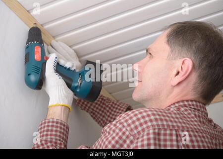 Contractor installing molding to ceiling using cordless power screw driver Stock Photo