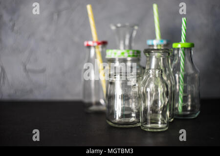 Different shape empty vintage bottles with and without lids and straw standing on black table with grey wall as background Stock Photo