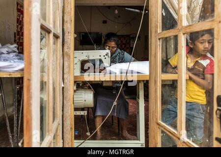 Kandy, Sri Lanka. 15th Feb, 2018. Thursday, February 15, 2018.SUDARSHANTI MANIKE sews bags for Self Employment Education & Welfare Association (SEWA), as her 7-year-old son peers out the window of their home near Kandy, Sri Lanka. MANIKE, a former garment factory worker, is happy because she can earn money for her childrens' education while being free to set her own hours and work at her own pace. Working for herself allows her the freedom to be with her children while she is sewing, tend her garden periodically and move about freely as she desires. She has been sewing bags for SEWA for Stock Photo