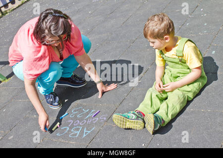 Mom and cute boy draw alphabet with colorful chalks on asphalt. Summer activity and creative games for small kids. Family time. Happy mother’s day. Stock Photo