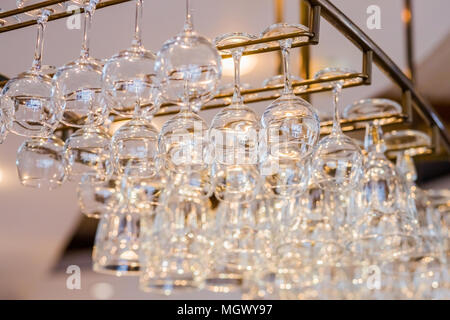 different glasses hanging over the bar.selective focus.horizontal low angle image of glasses stacked on metal hanging bar glass racks in a club or a restaurant with yellow light bulbs shining above them Stock Photo
