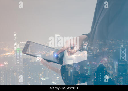 Double exposure concept businessman wearing black suit and working with a digital tablet with modern city night background. Stock Photo