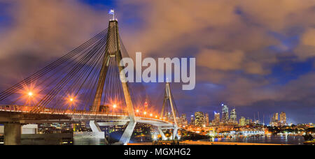 Anzac bridge with flags of Australia and New zeland on top gates with steel cables in front of Sydney city CBD urban towers at sunset with bright illu Stock Photo