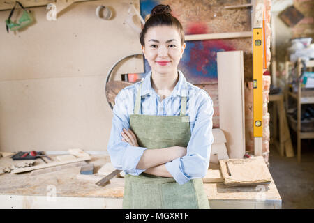 Waist up portrait of young female artisan posing in crafting shop standing with arms crossed, looking at camera and smiling, copy space Stock Photo