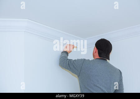 Installation of ceiling moldings. Worker fixes the wood molding to the ceiling Stock Photo