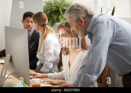 Aged executive manager supervising computer work of intern in of Stock Photo