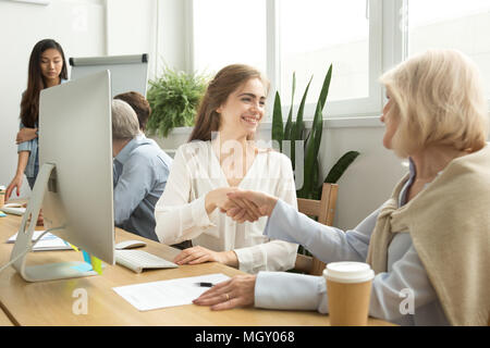 Smiling young and senior businesswomen shaking hands in coworkin Stock Photo