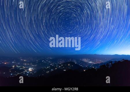 Night sky star trails around the North star with city lights in the background taken from the top of a hill in himalayas Stock Photo