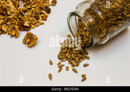 Vintage glass jar full with peeled sunflower seeds and walnuts. Food spilled and isolated on white background with space to ad text or elements. Stock Photo