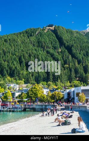 view of the queenstown skyline gondola queenstown hill from the sandy beach on lake wakatipu shore lakeside queenstown South Island New Zealand nz Stock Photo