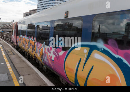 Brightly coloured graffiti on the side of a south western railway train in a platform at london waterloo station. Railway crime and vandalism of train Stock Photo