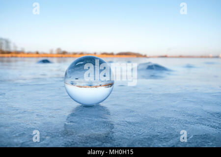 Transparent glass orb on a frozen lake with ice in the winter Stock Photo